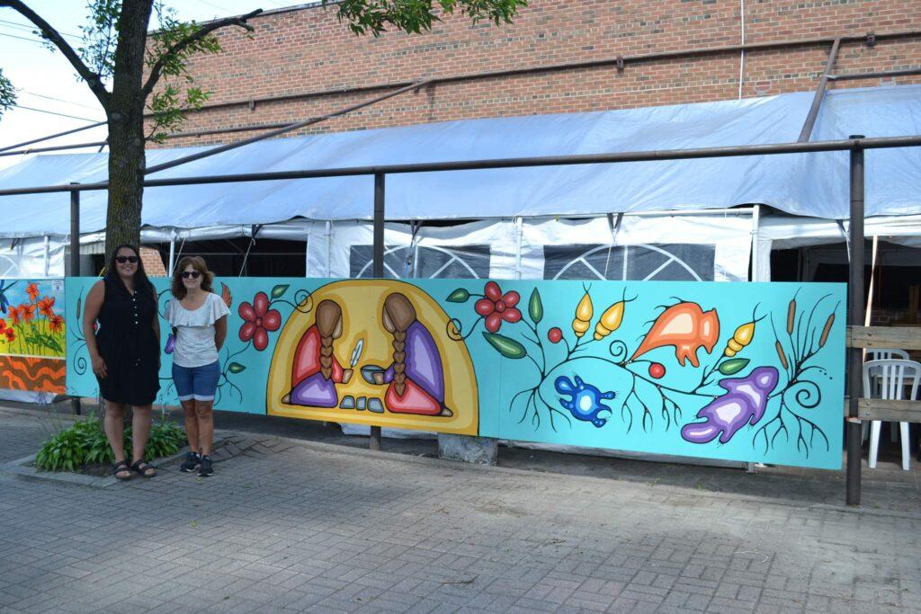 Jules Armstrong stands in front of her mural depicting Seven Grandfather Teachings.