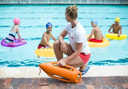 Lifeguard holding rescue can while children swimming in pool