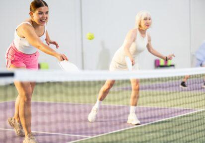 Girl playing doubles pickleball in team with older woman indoors